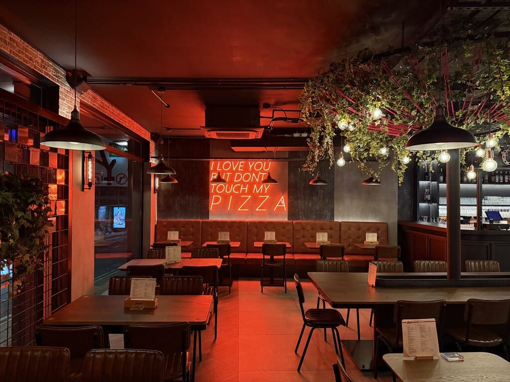 Japes Camden dining room with red lighting, hanging plants and a pizza neon sign