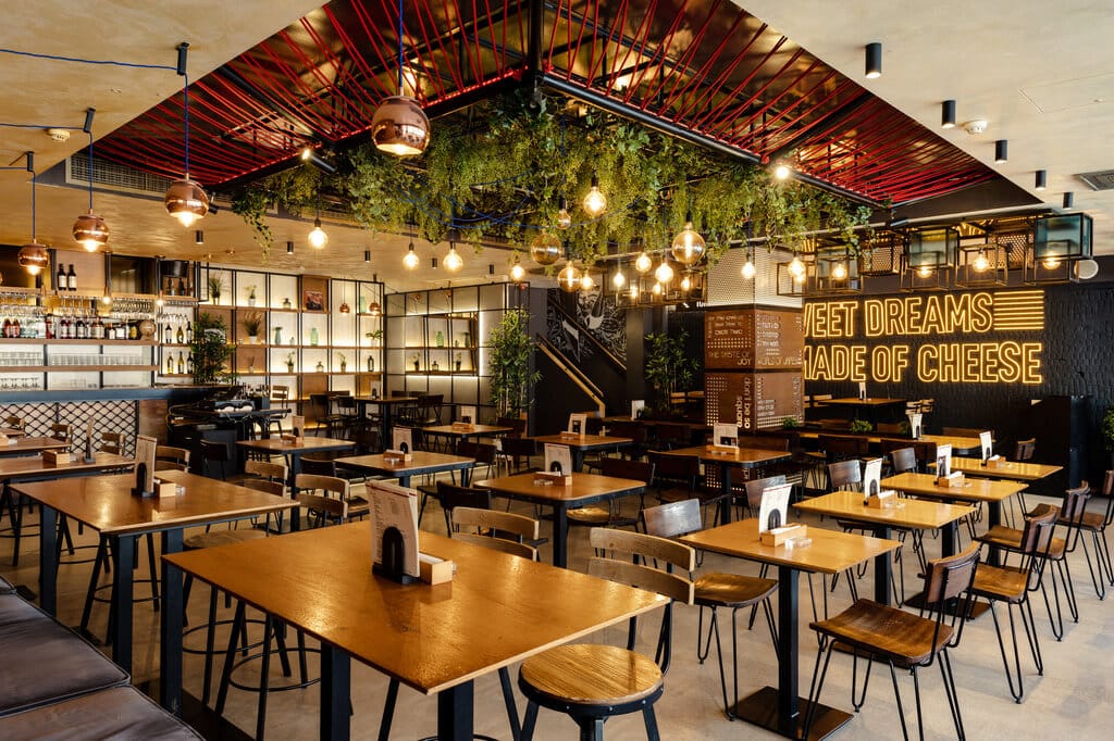 Japes Soho dining room with hanging greenery, wooden tables and a neon sign